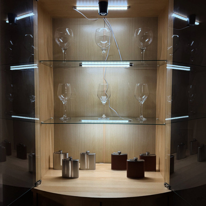 Glass display cabinet with wine glasses and small containers on a dark background